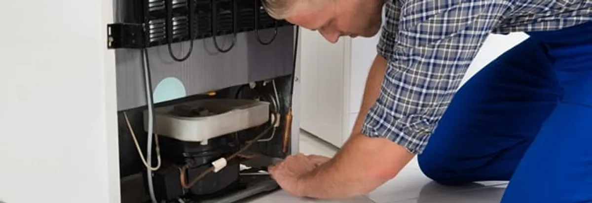 Refrigerator repair technician servicing the compressor and condenser area in Kansas City, KS
