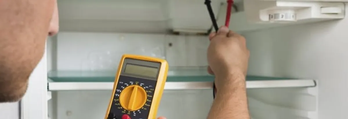 Refrigerator repair technician testing electrical components with a multimeter in Kansas City, KS